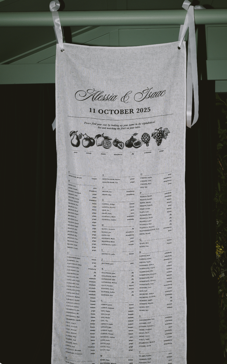 Wedding seating chart with illustrations of fruits and table assignments for Alexandra and Isaac, dated October 11, 2025.