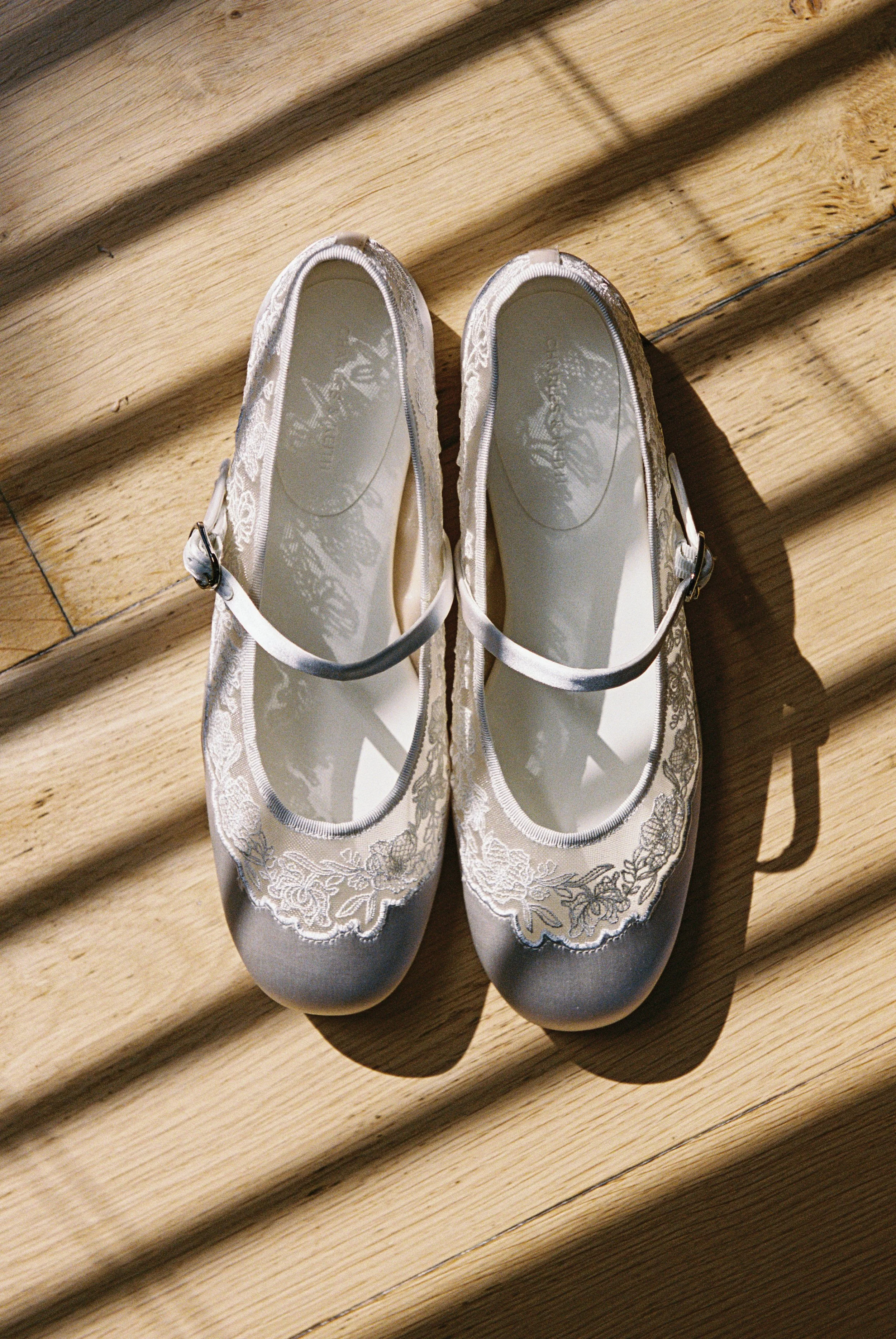 Pair of white ballet shoes with lace embroidery on a wooden floor.