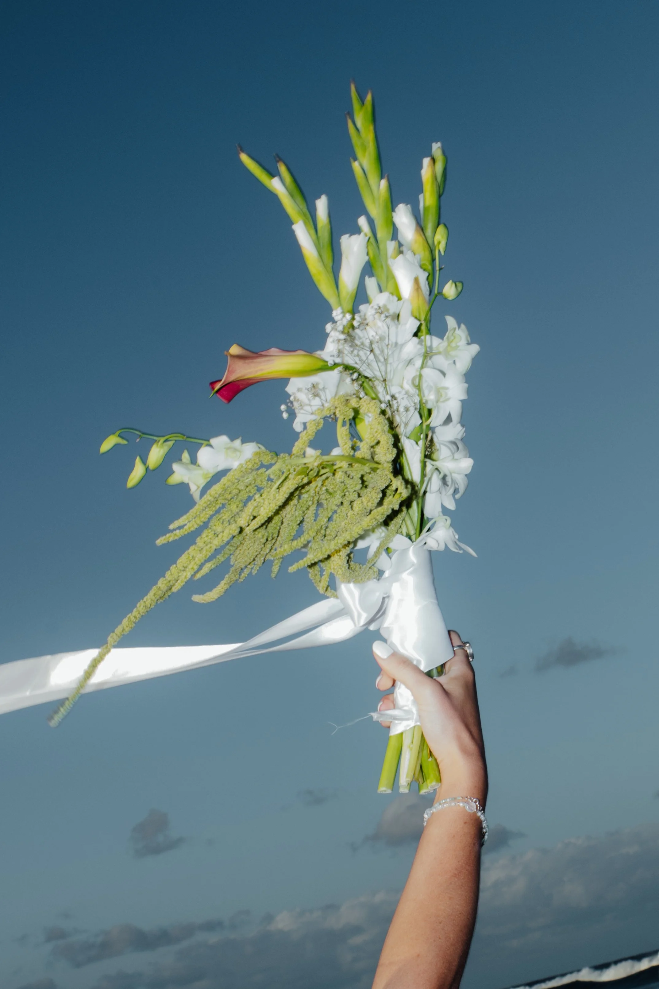A person holding a bouquet of white and green flowers against a blue sky with some clouds.