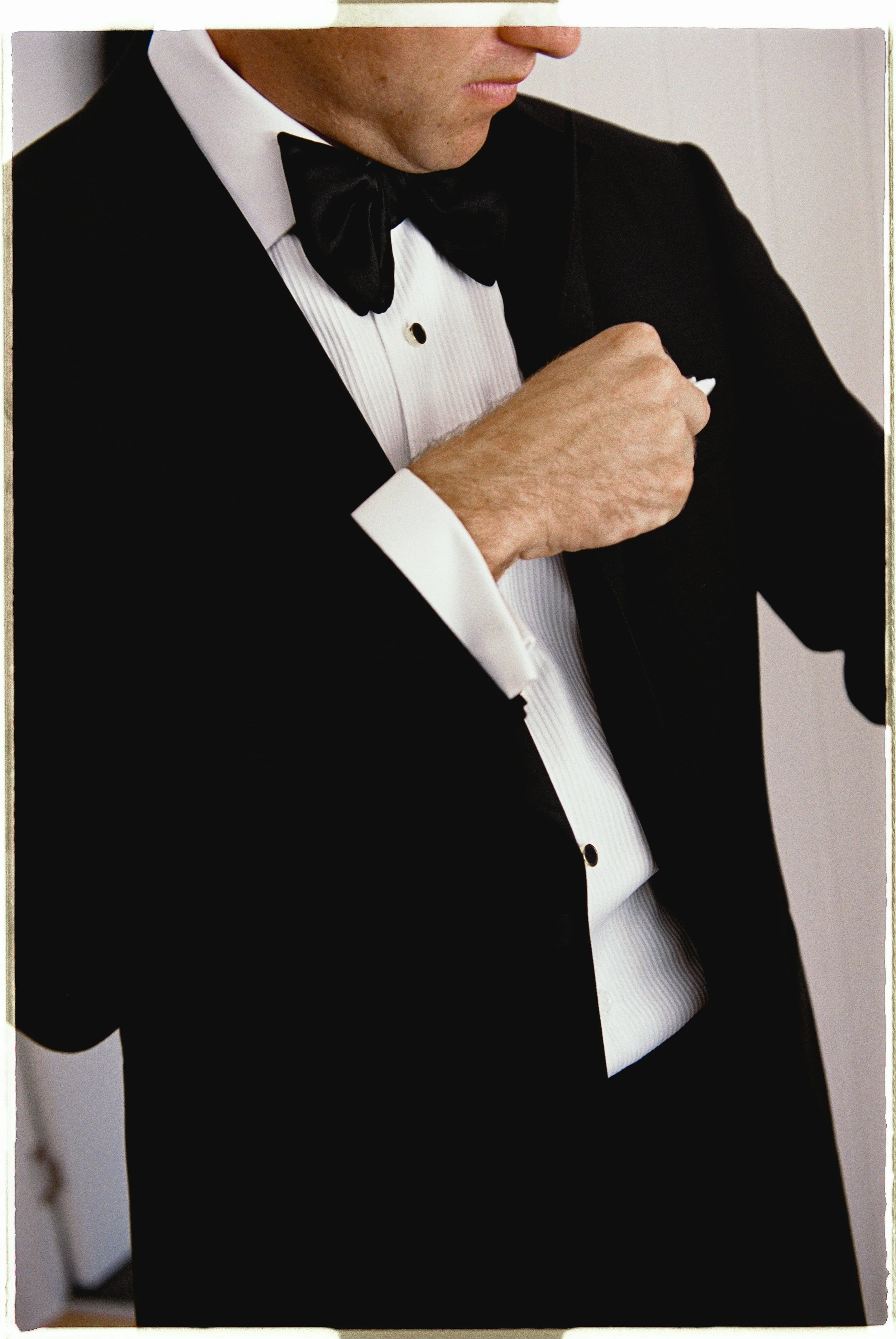 A man in a tuxedo adjusting his black bow tie.