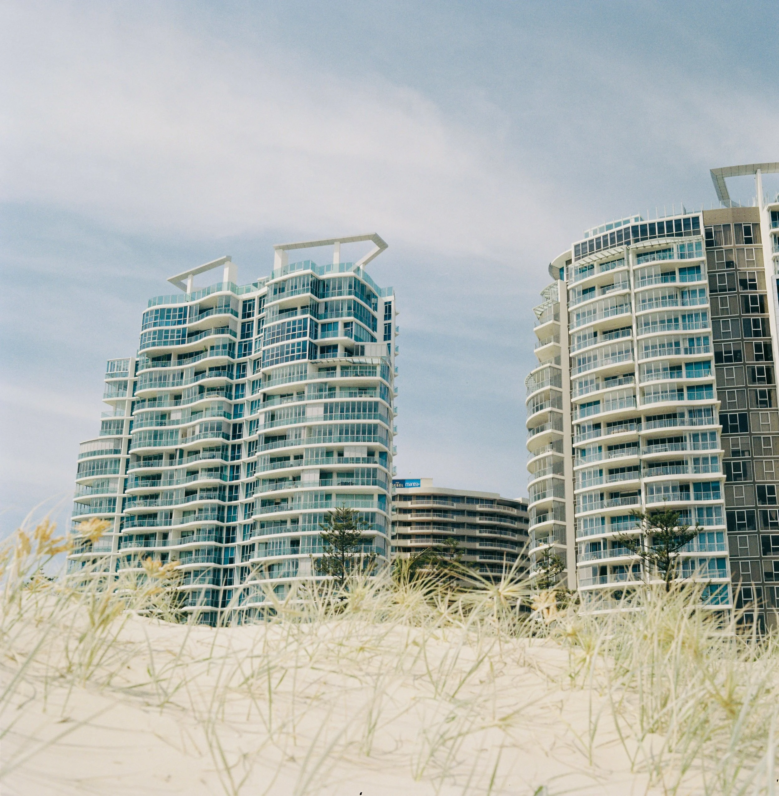 View of modern high-rise apartment buildings near the beach with grassy dunes in the foreground.