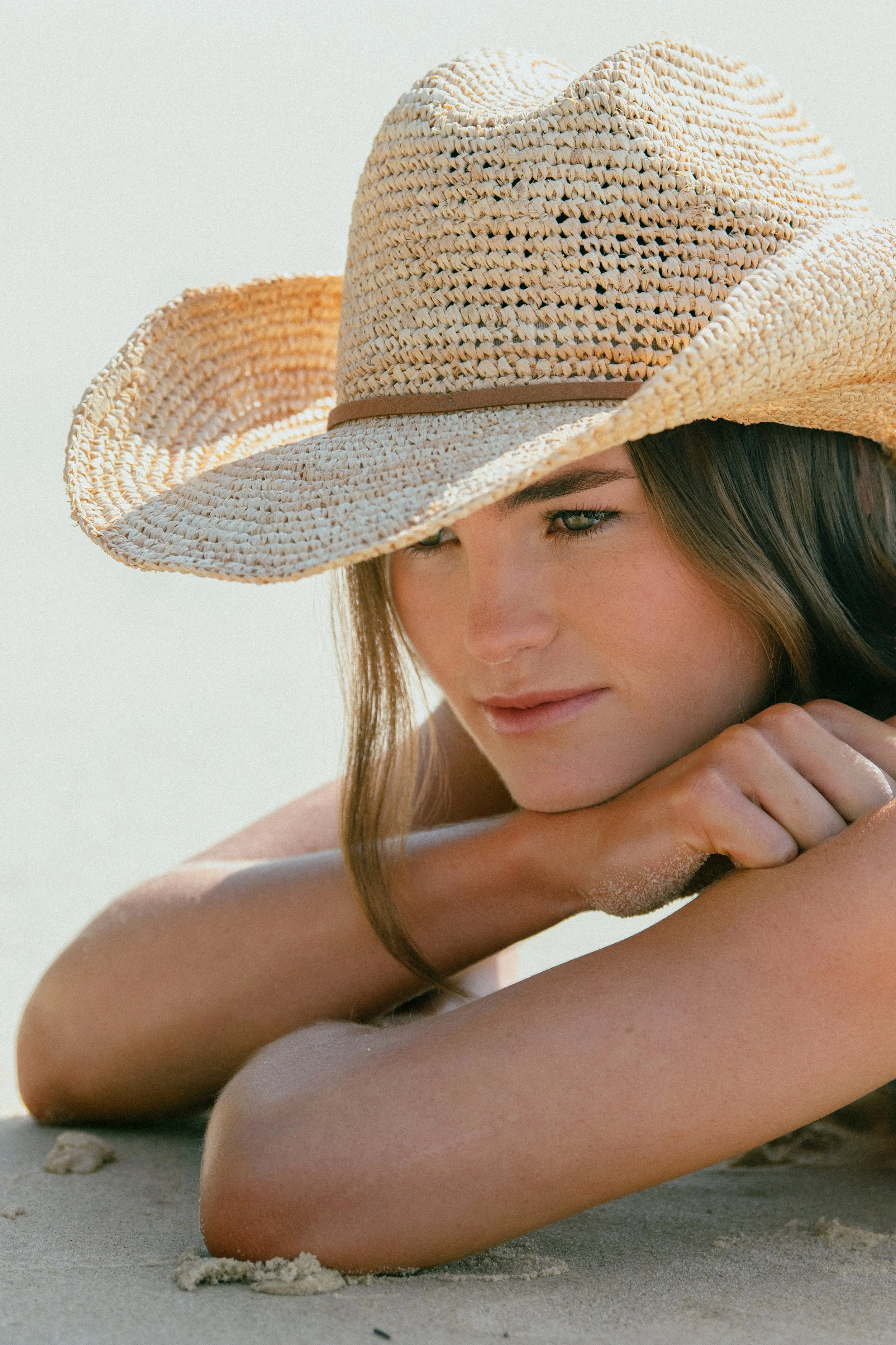 A woman lying on the sand, wearing a wide-brimmed straw hat.