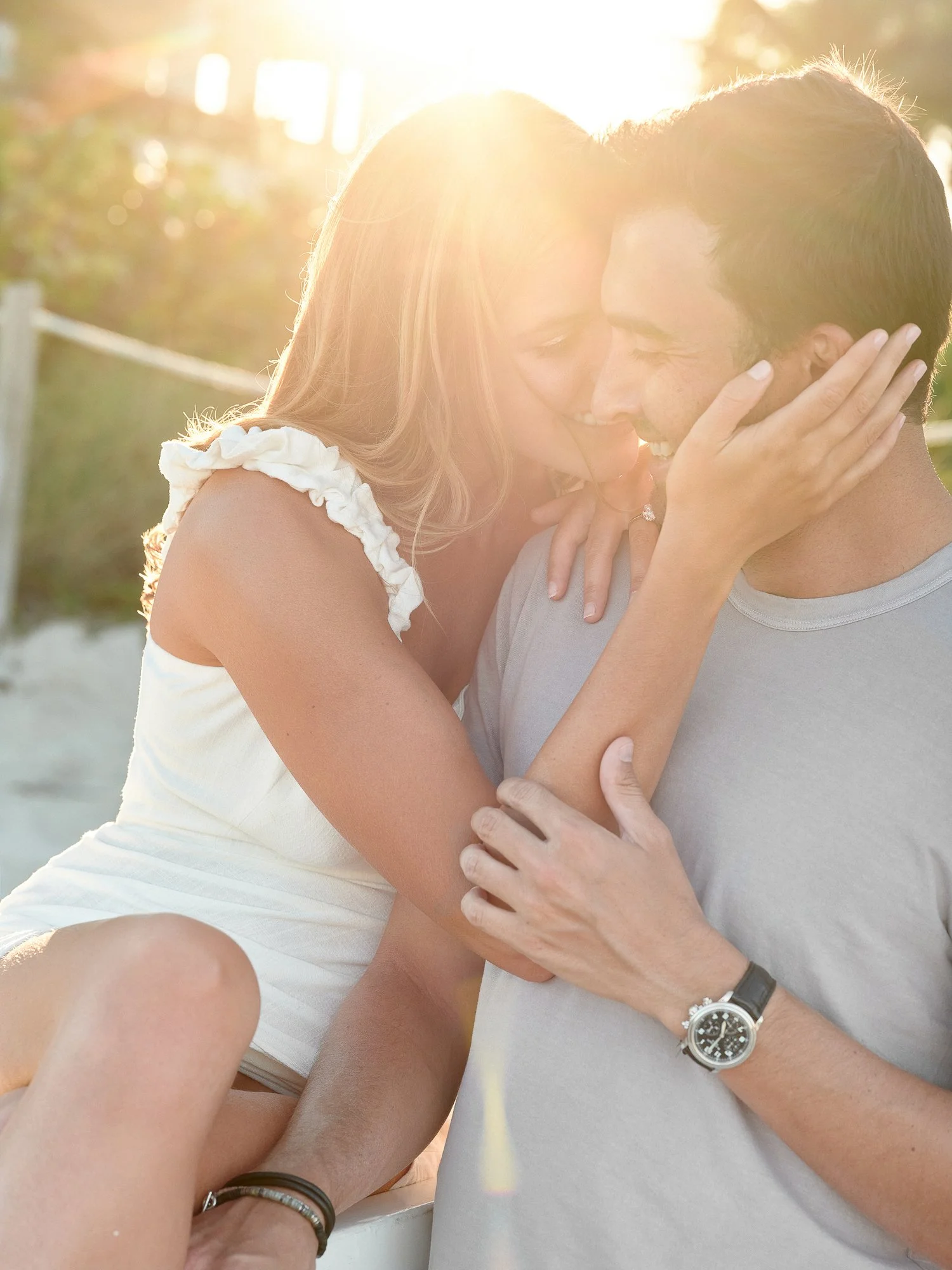A couple sharing an intimate moment outdoors during sunset, with the woman touching the man's face and both smiling with closed eyes.