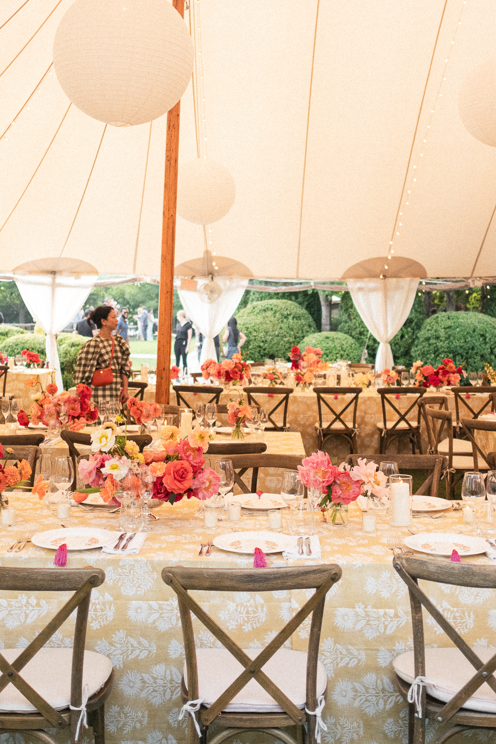 A decorated outdoor event tent with tables adorned with pink and peach floral arrangements for a celebration or wedding reception.