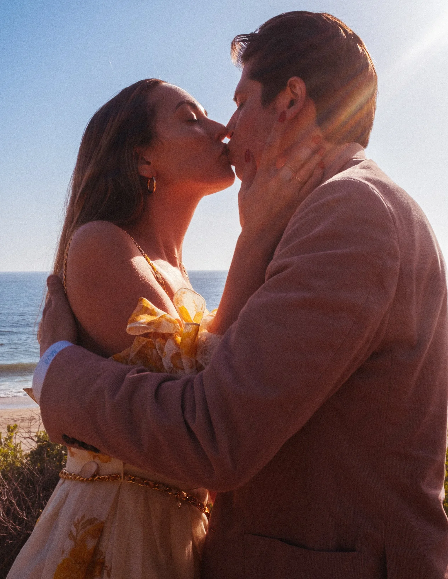 A couple kissing on a beach during sunset, with the ocean in the background.