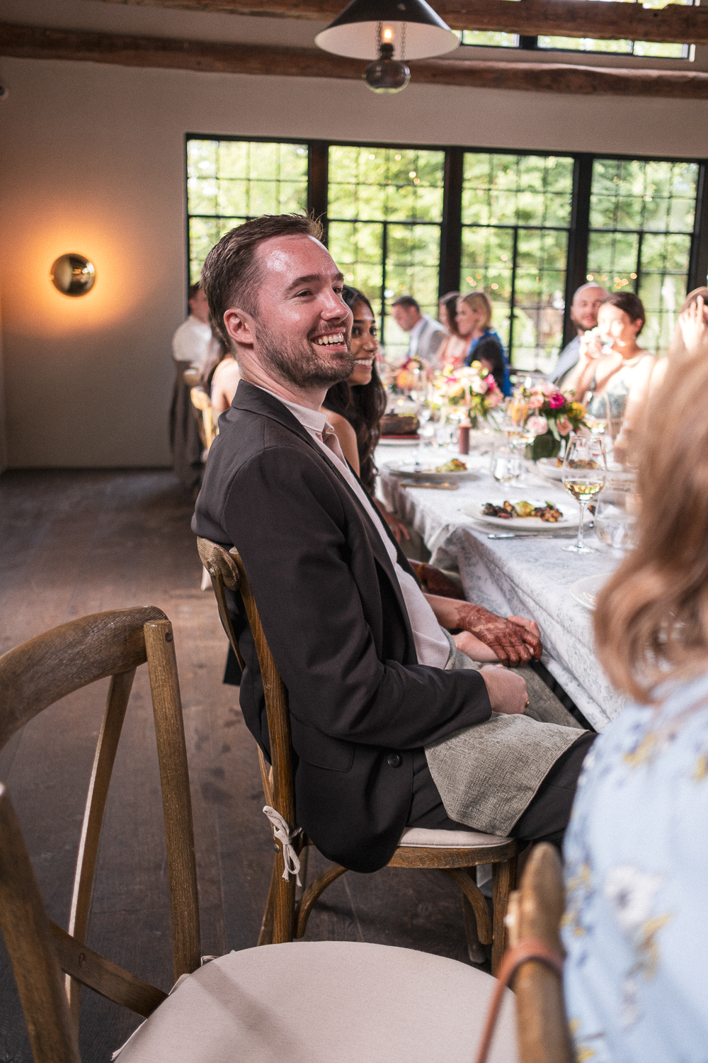 People sitting at a long dining table with flowers, enjoying a celebration in a bright room with large windows.