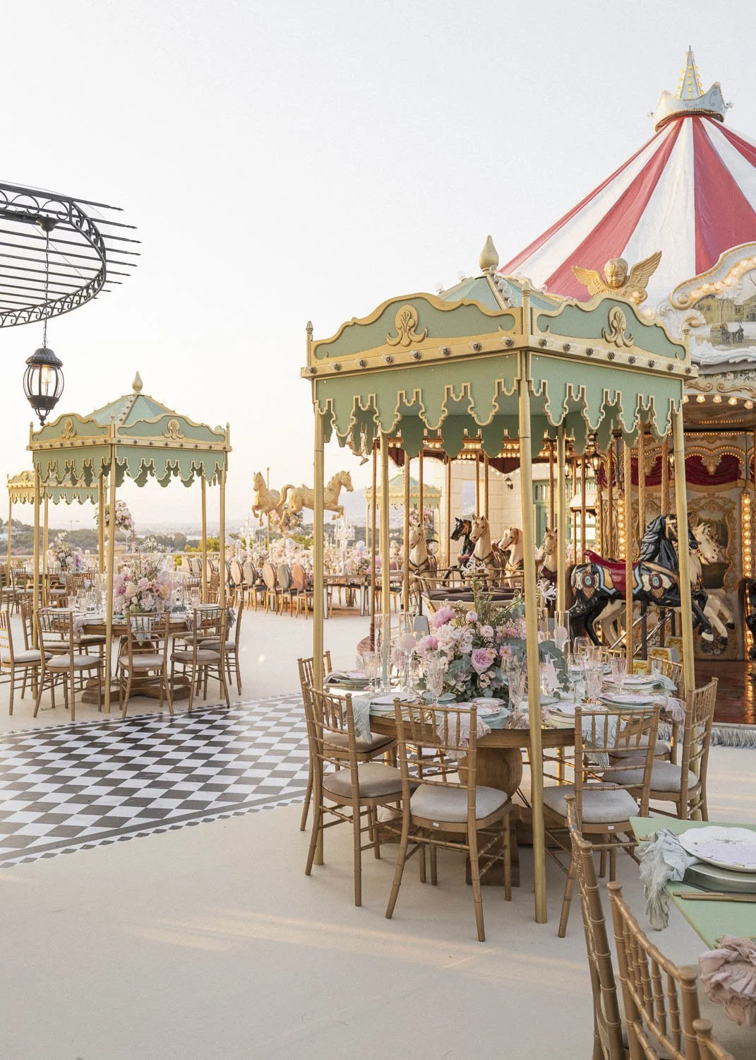 Outdoor carnival-themed event setup with decorated tables, floral centerpieces, carousel horses, and vintage carousel rides.