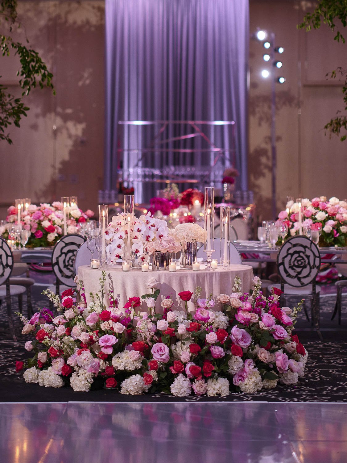 Elegant indoor event decorated with pink and white flowers, candles, and table settings, featuring a grand piano in the background.