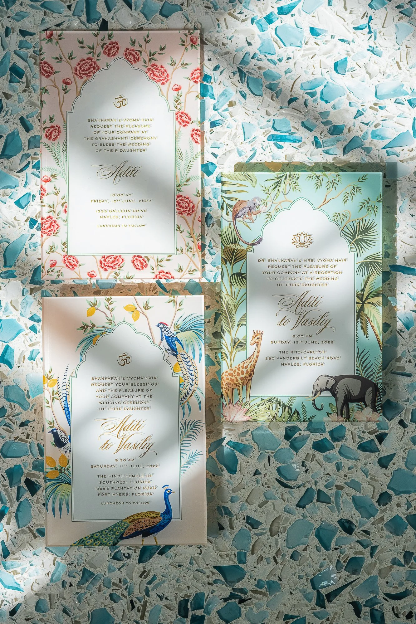 Three wedding invitations on a terrazzo surface with blue, white, and gray chips. Each invitation features floral or animal illustrations with elegant text.