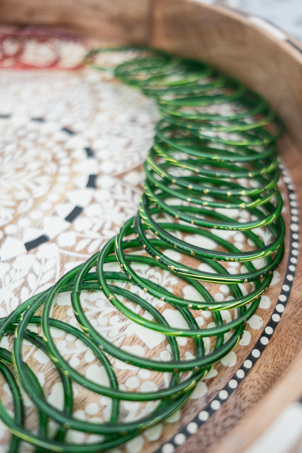 A row of green bangles with gold accents on a decorative tray.