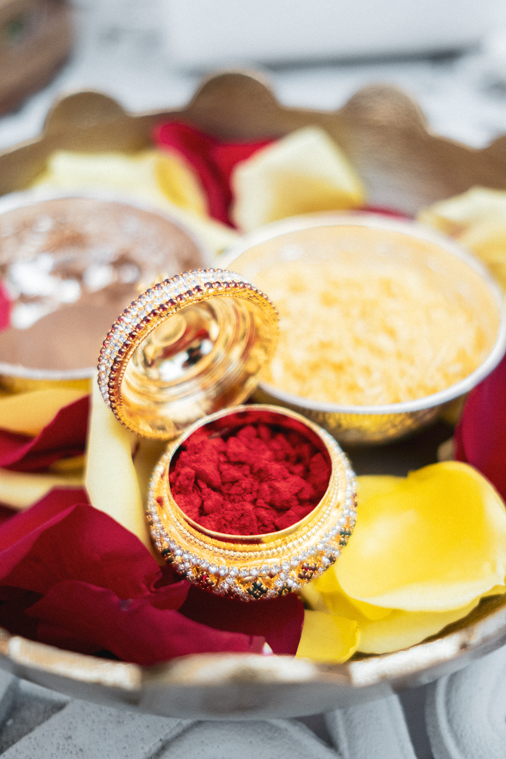 Decorative gold containers filled with red, yellow, and orange powders, surrounded by red and yellow flower petals, on a floral tray.