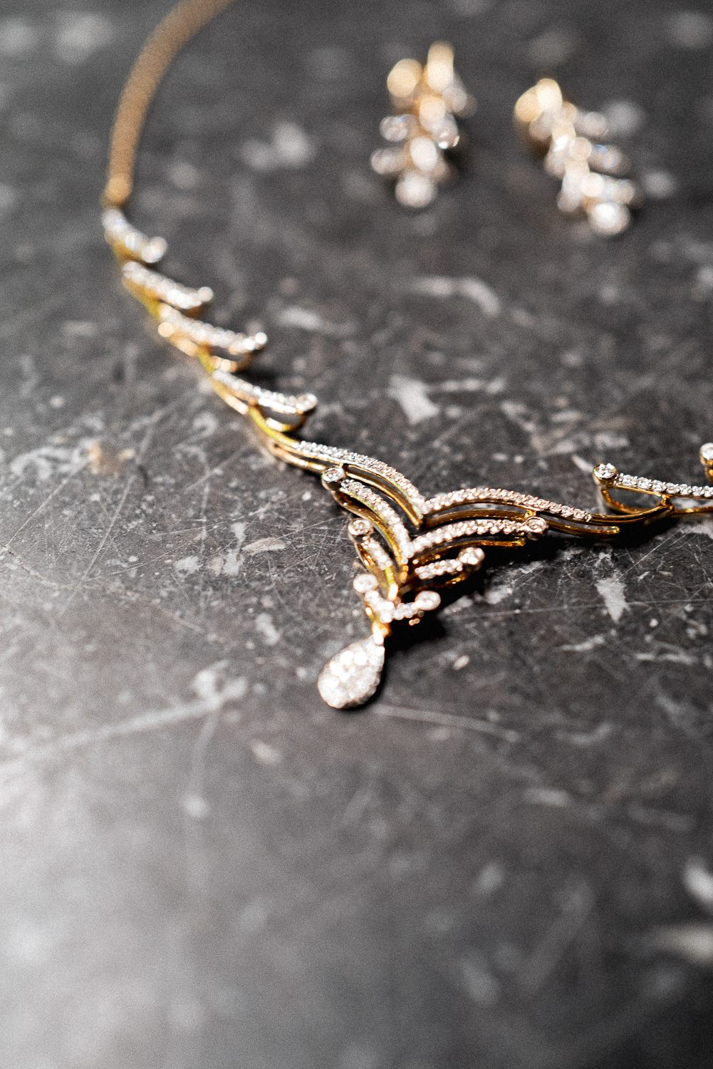 Close-up of gold jewelry with diamond accents, including a necklace and earrings, on a dark textured surface.