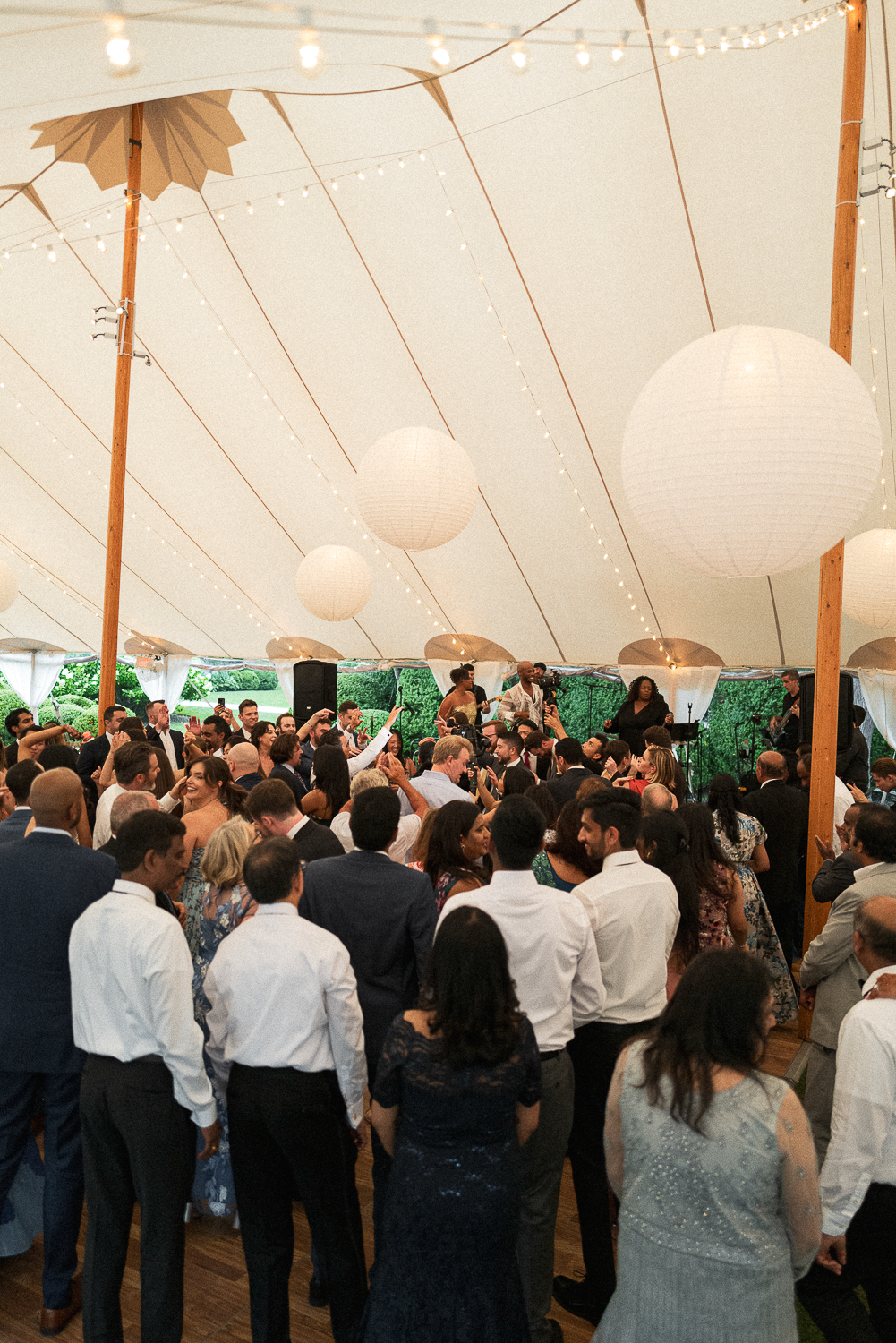 People dancing and enjoying live music under a large white tent decorated with string lights and paper lanterns.