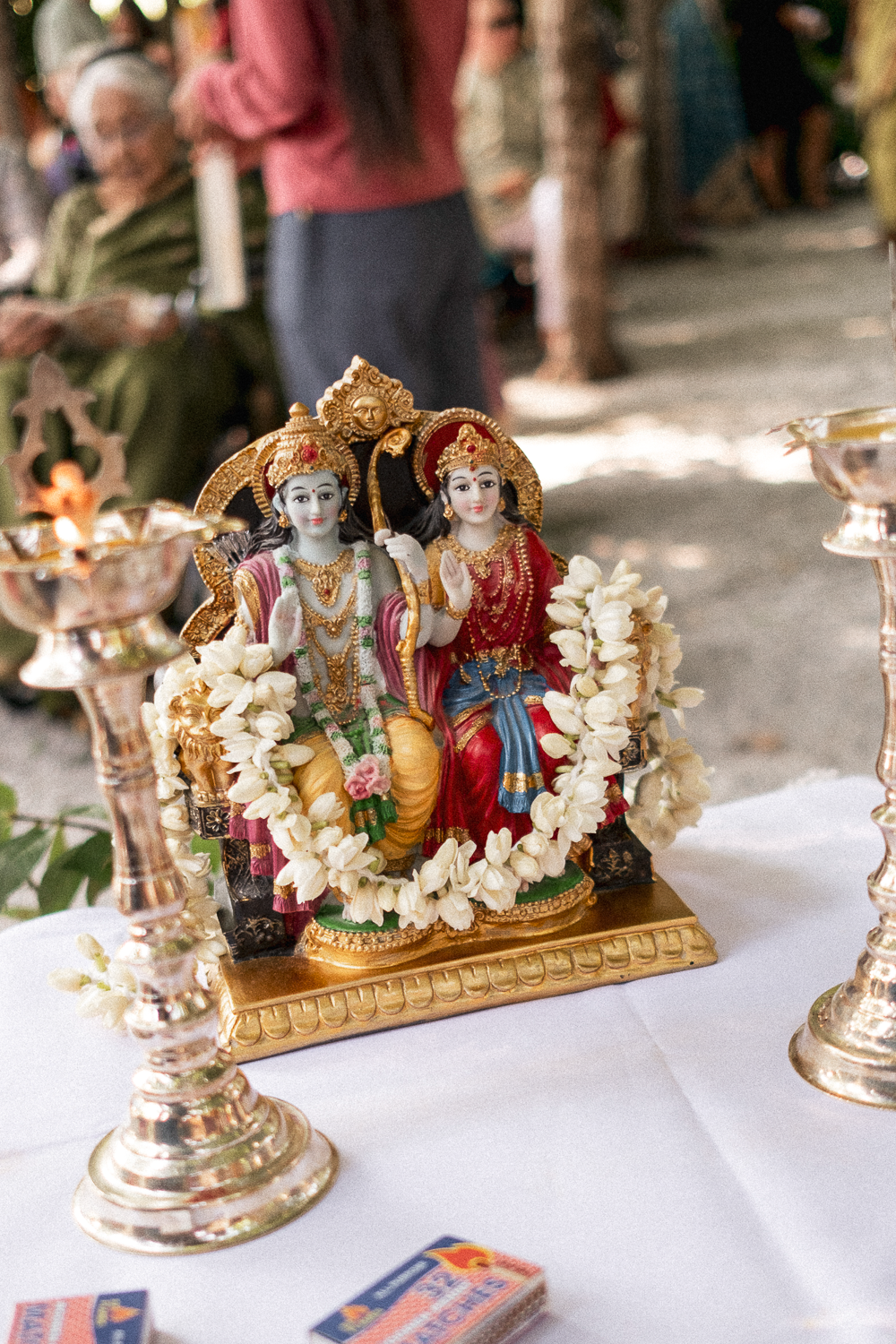 Hindu deity statues adorned with flowers, set on a table with candles, in an outdoor ritual setting.