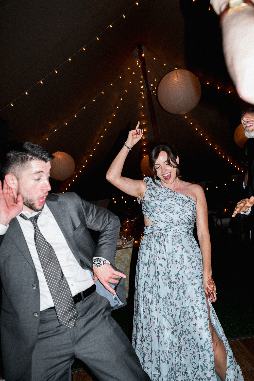 People dancing and celebrating at a party under string lights and paper lanterns.