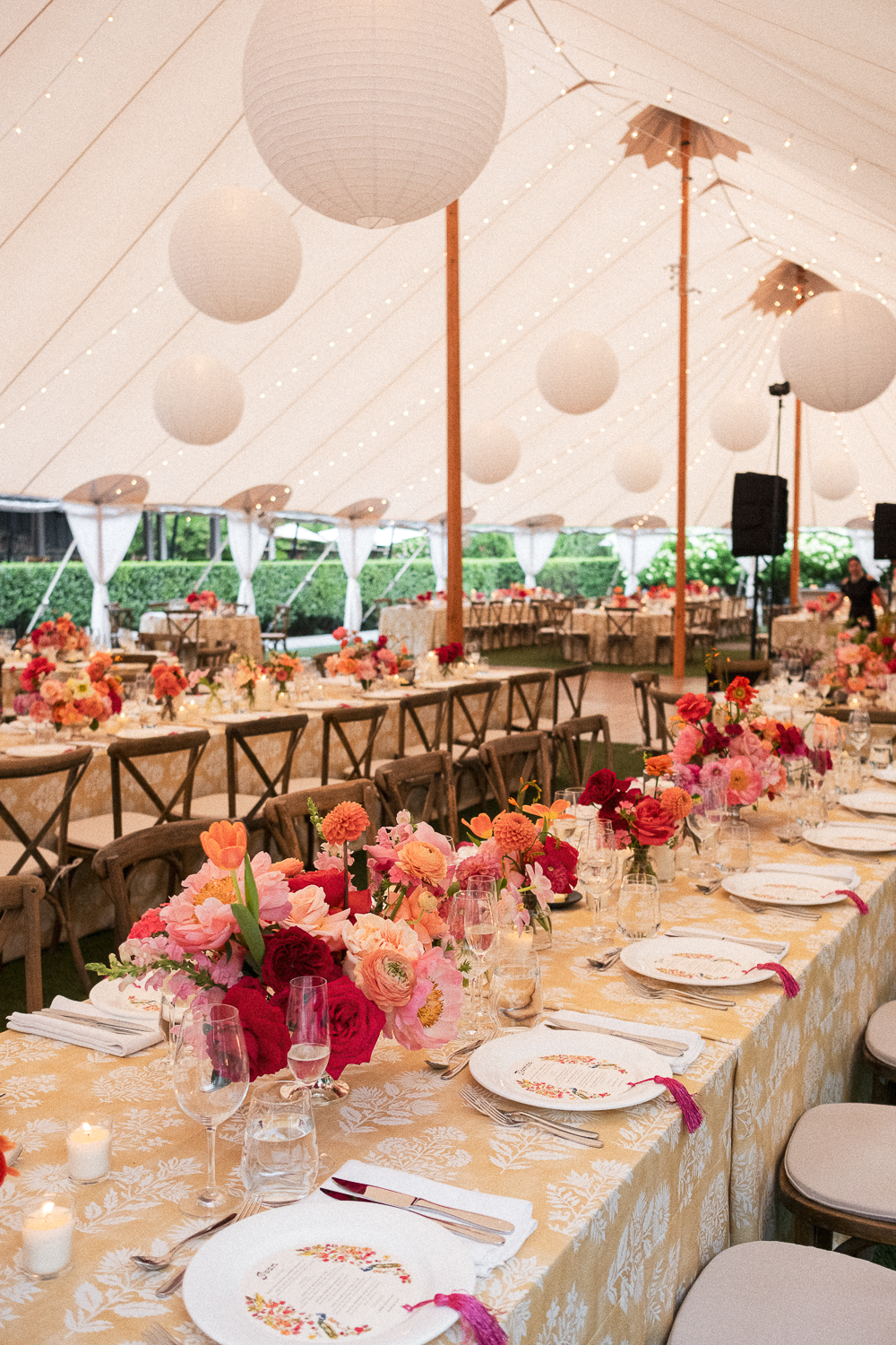 Decorated event tent with tables of floral arrangements, candles, and dinnerware.