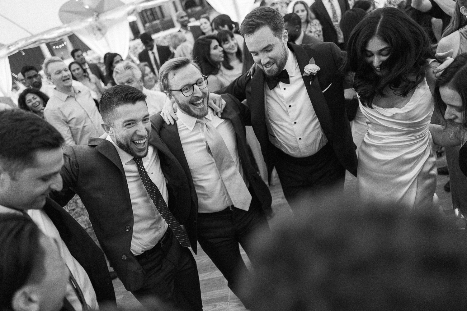 Group of people at a wedding reception dancing together in a circle, smiling and enjoying the moment.