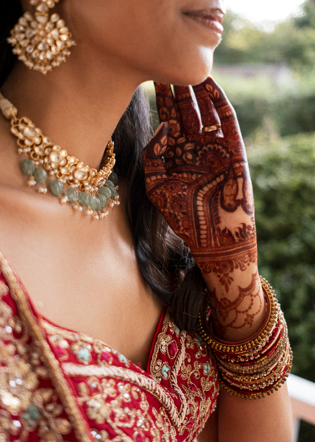 Close-up of a woman dressed in traditional Indian attire, wearing gold jewelry, bangles, and henna on her hand.