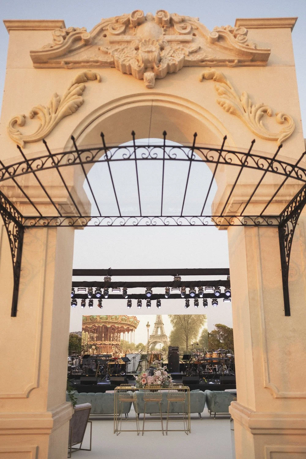 Elegant outdoor event setup with stage, musical instruments, and the Eiffel Tower replica in the background, viewed through a decorative archway.