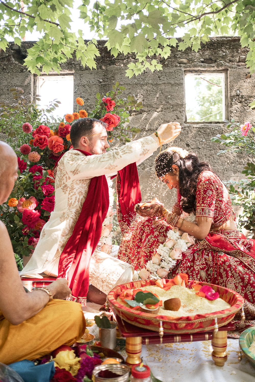 Indian wedding ritual with bride and groom dressed in traditional attire, surrounded by colorful flowers, during a ceremony.