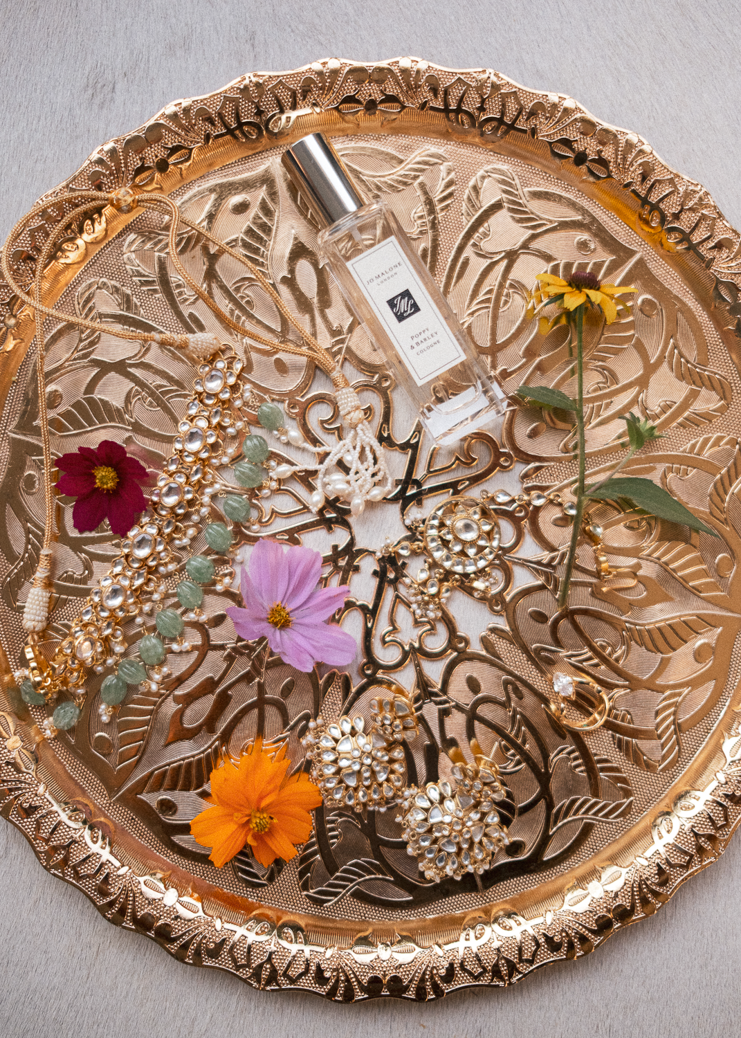 A round ornate gold tray filled with jewelry, flowers, and a perfume bottle.