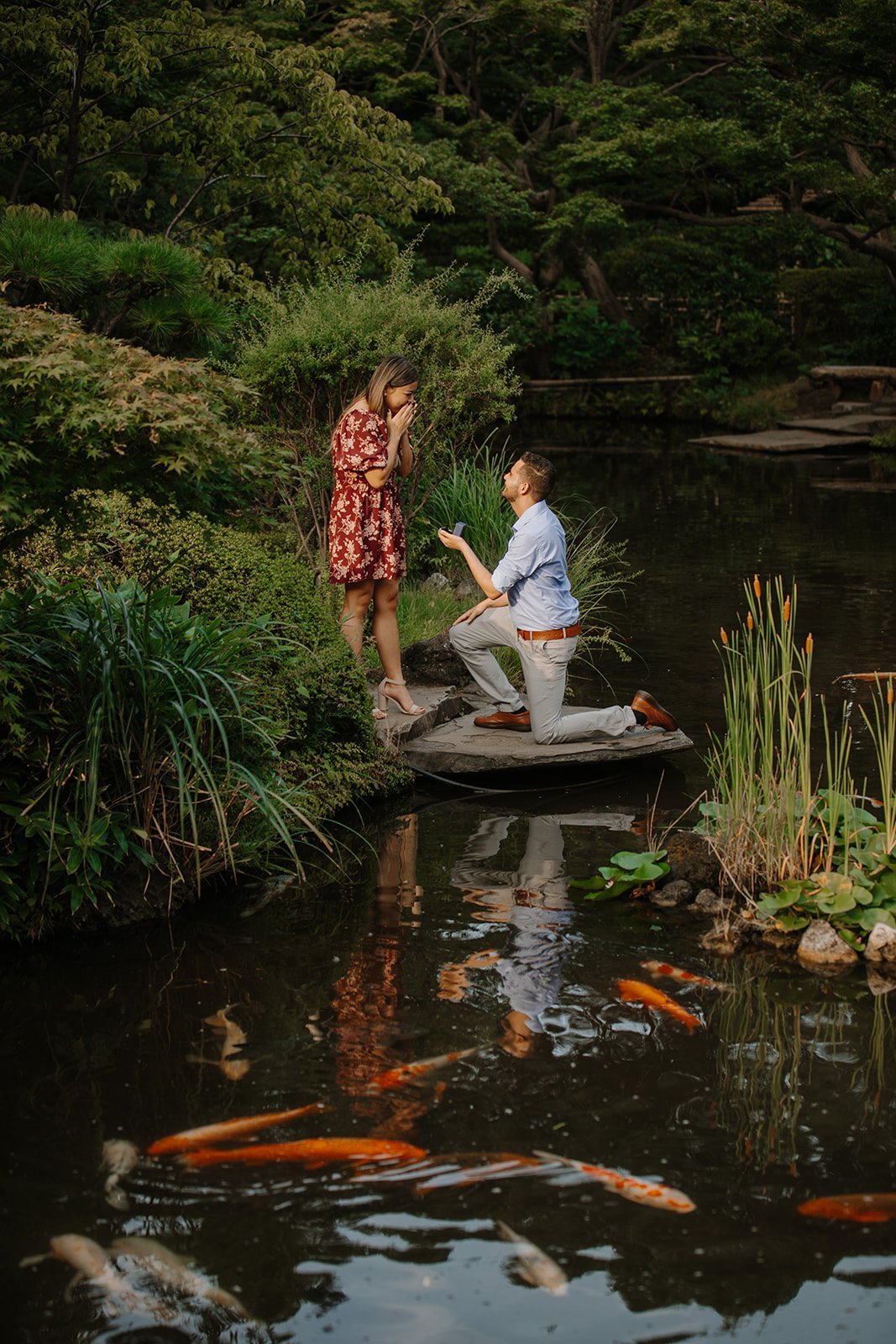 Woman reacting in surprise as her partner kneels to propose beside a koi pond in a Tokyo garden