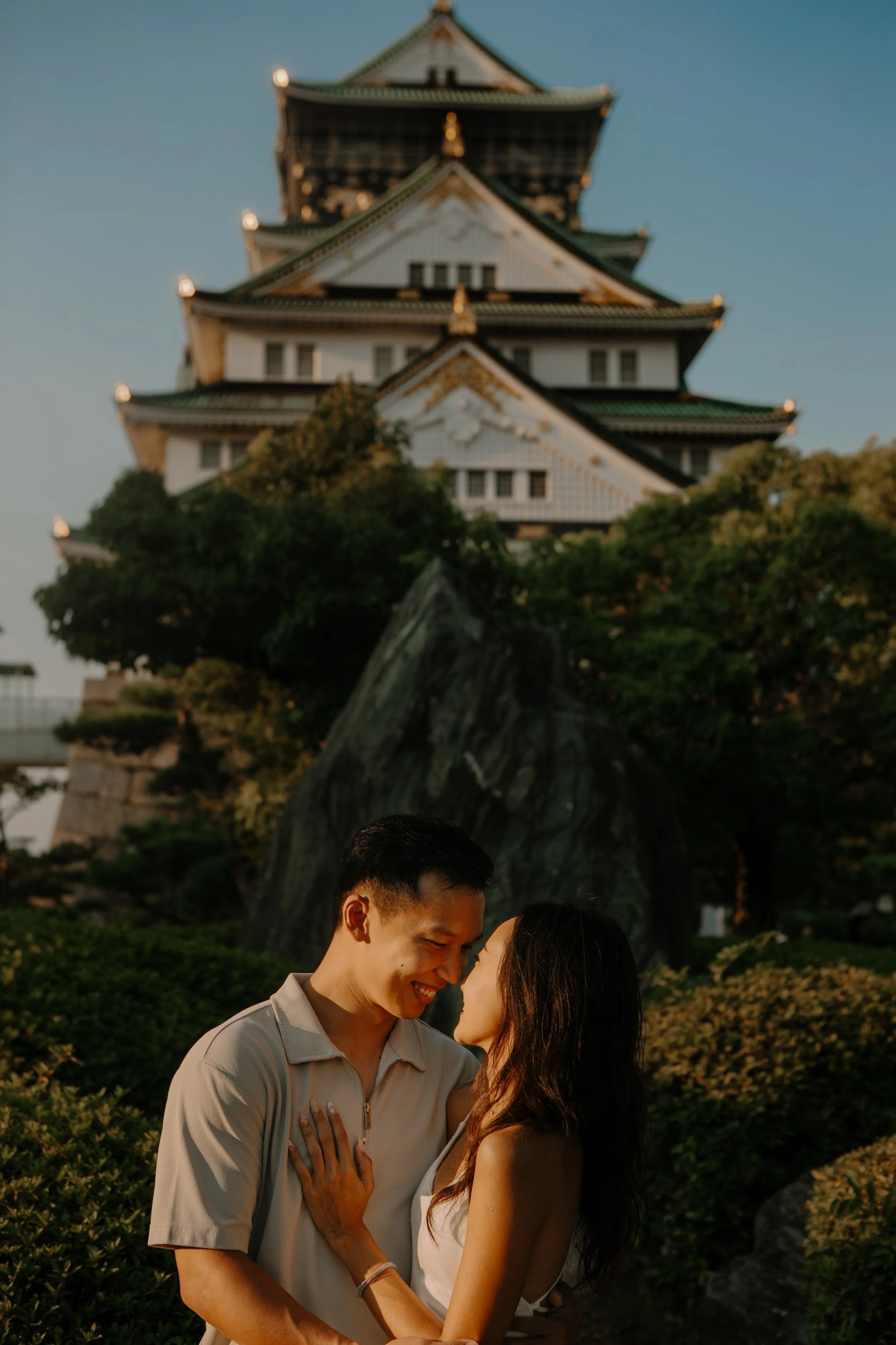 Couple touching foreheads with Osaka Castle glowing gold at sunset behind them