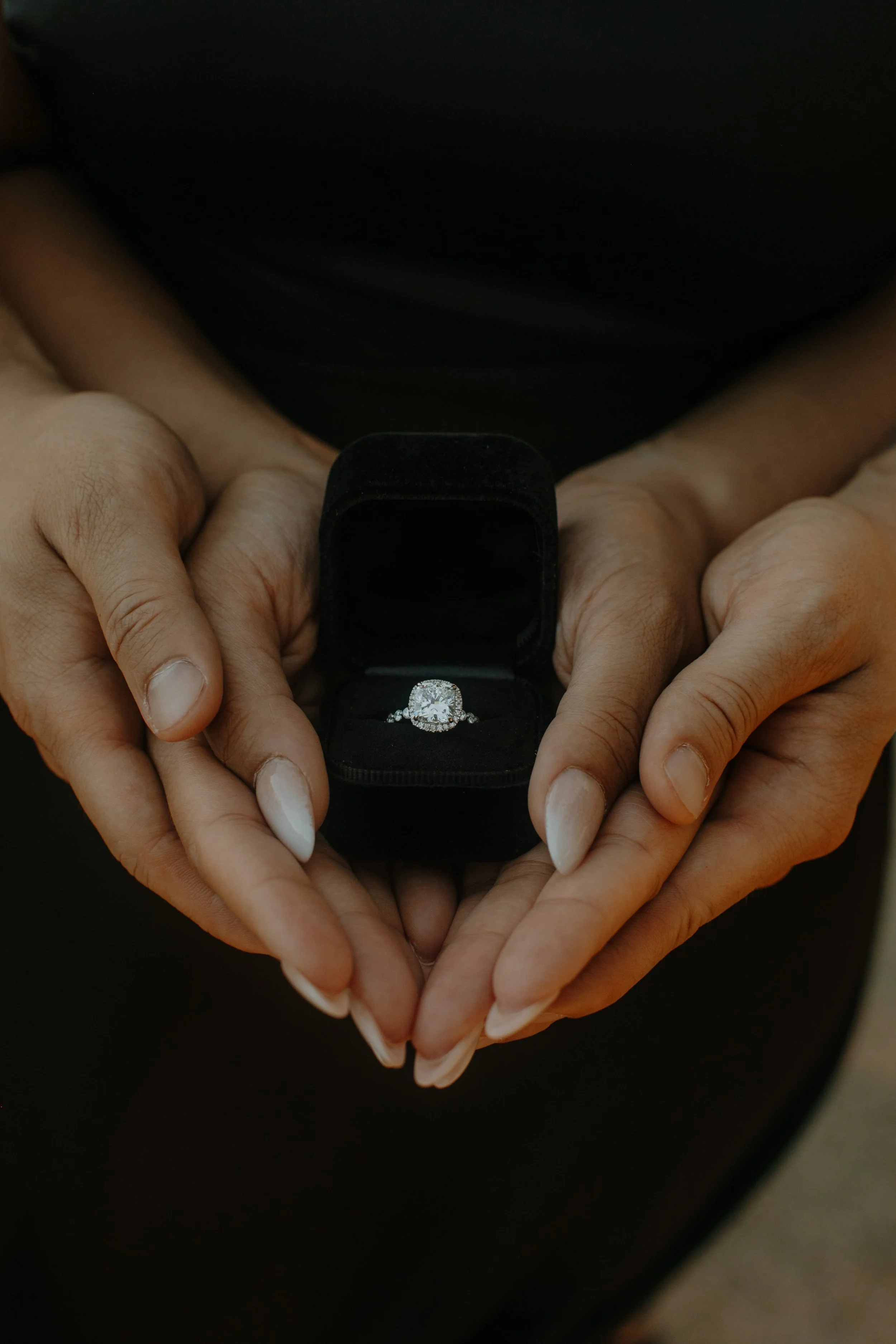 Close-up of a woman's hands cupping an open ring box with a diamond engagement ring inside