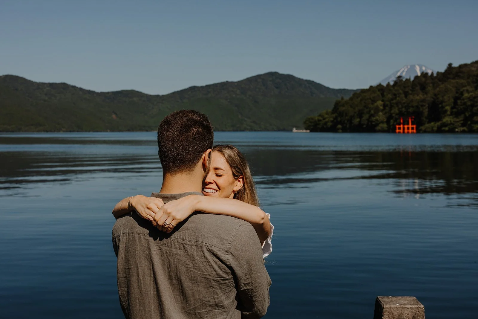 Couple embracing with their backs to the camera on the shore of Lake Ashi, Mount Fuji in view, Hakone, Japan