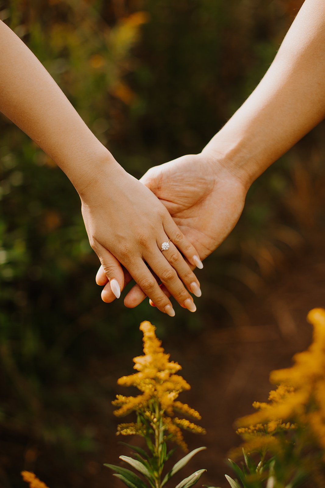 Detail of the couple's intertwined hands and diamond ring framed by golden wildflowers.