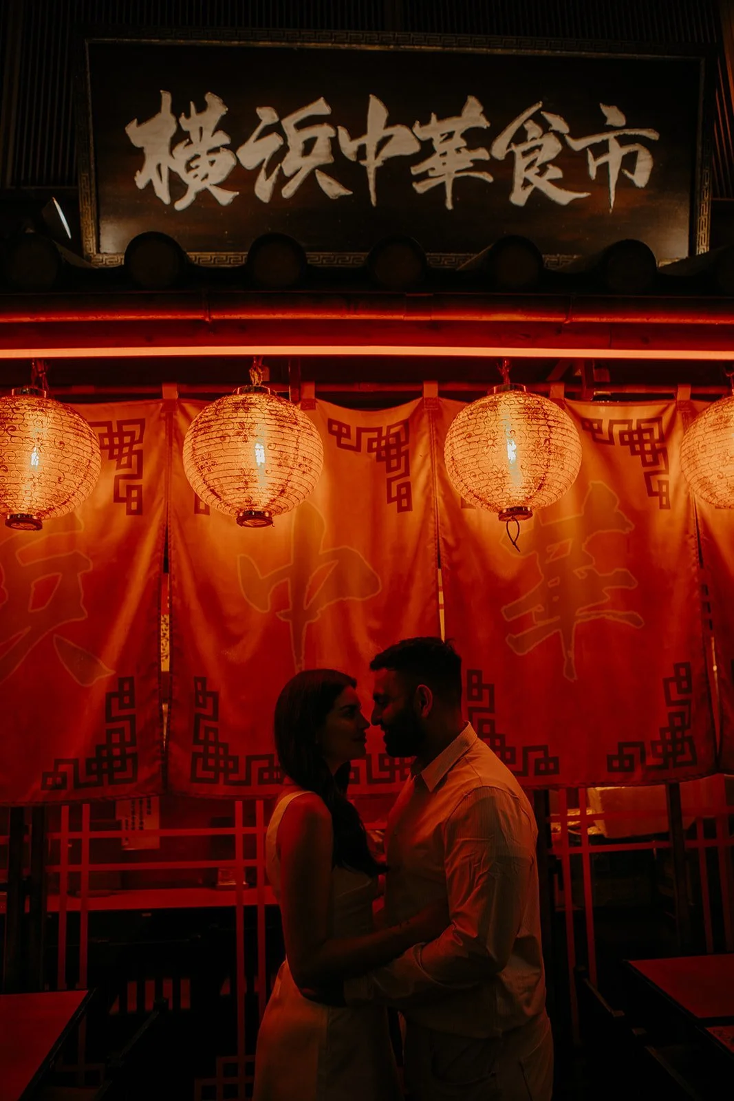 Silhouette of an engaged couple standing close beneath red lanterns in a Yokohama Chinatown alley