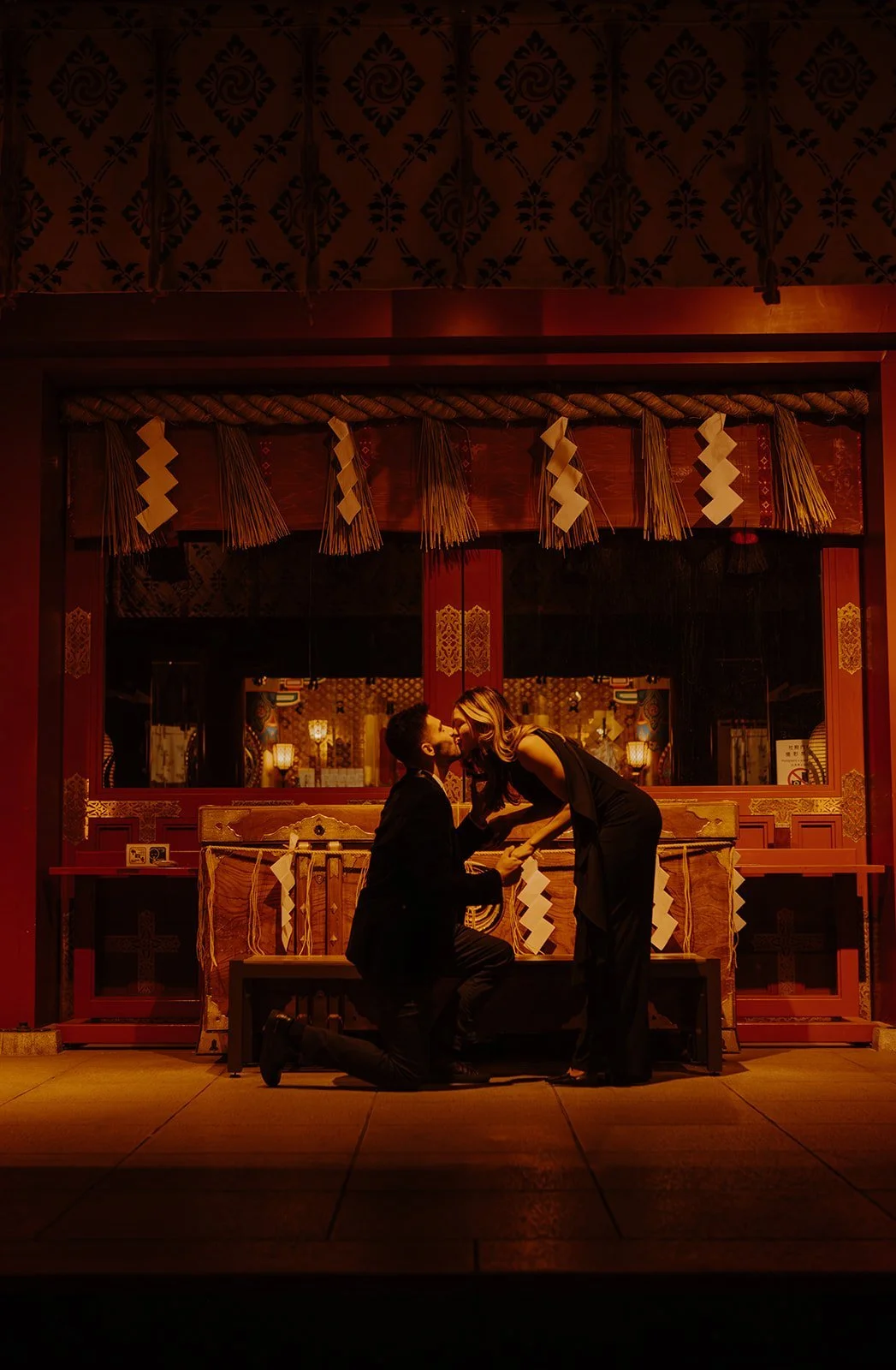 Newly engaged couple kissing beside the offering hall at Kanda Myojin Shrine in Tokyo at night