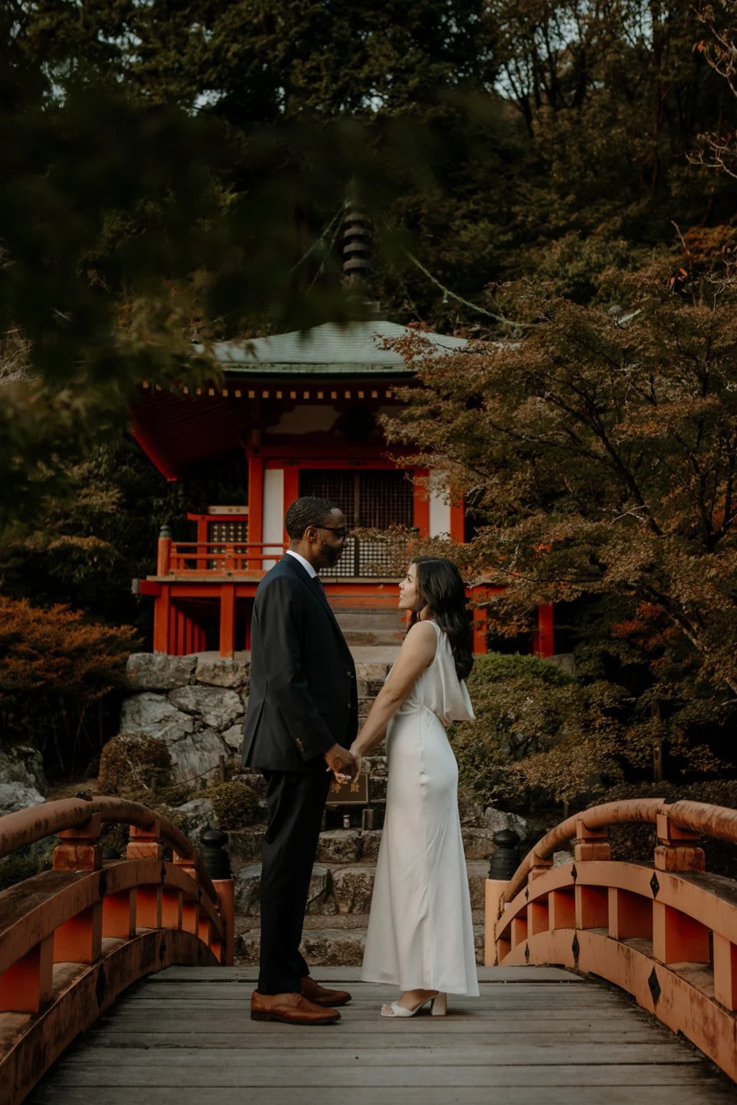 Couple faces each other on the red wooden bridge at Daigo-ji temple in Kyoto.