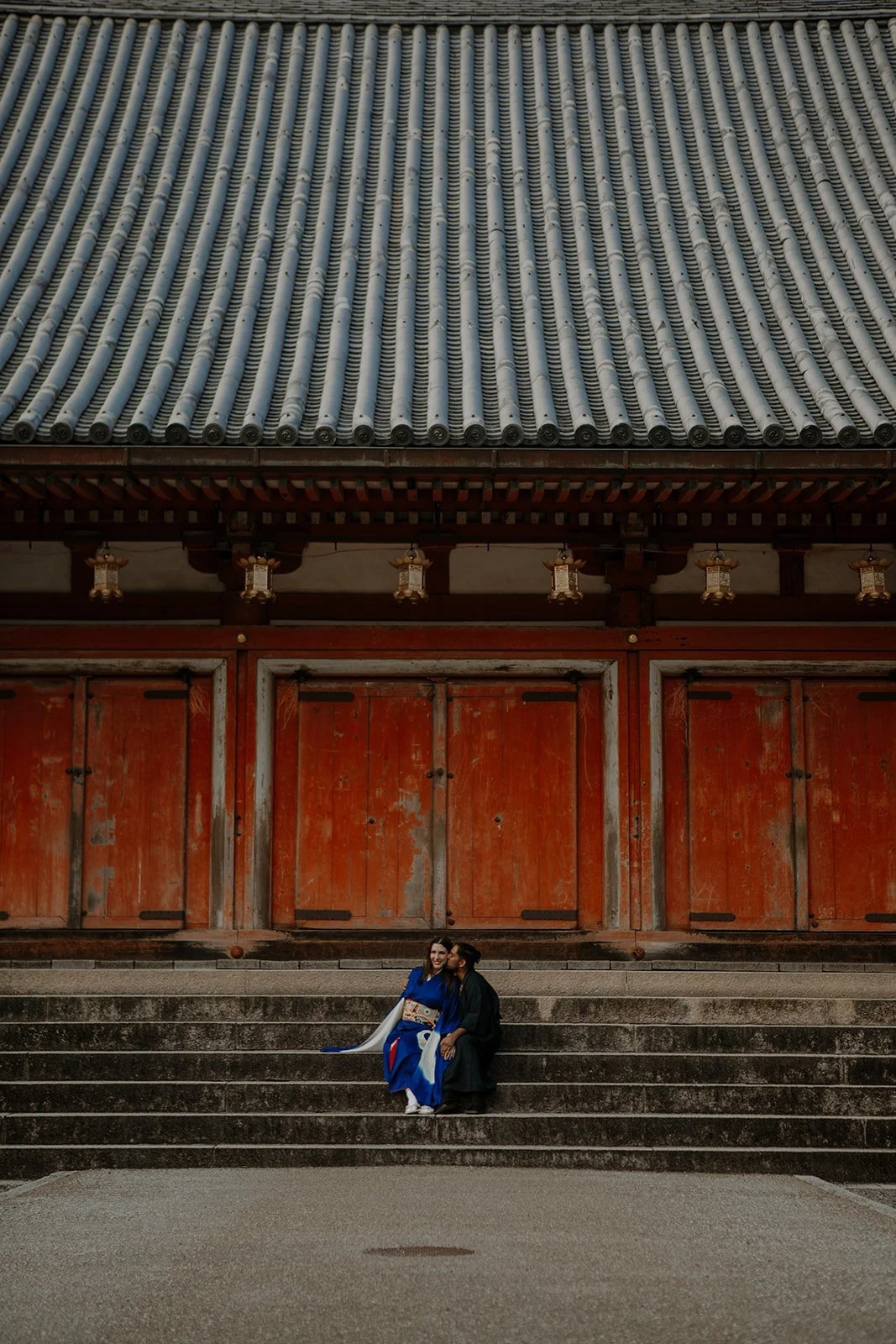 Couple in traditional kimono sitting together on the stone steps of a red temple gate in Kyoto, Japan