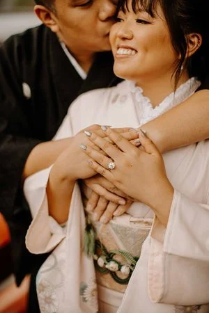 Close-up of a smiling woman in kimono being kissed on the forehead, her engagement ring visible on her hand