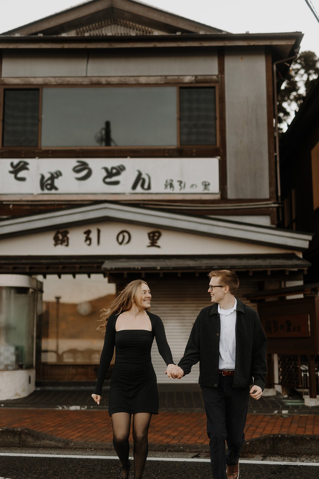 Couple laughing and holding hands as they walk past a traditional soba and udon shopfront in Hakone town