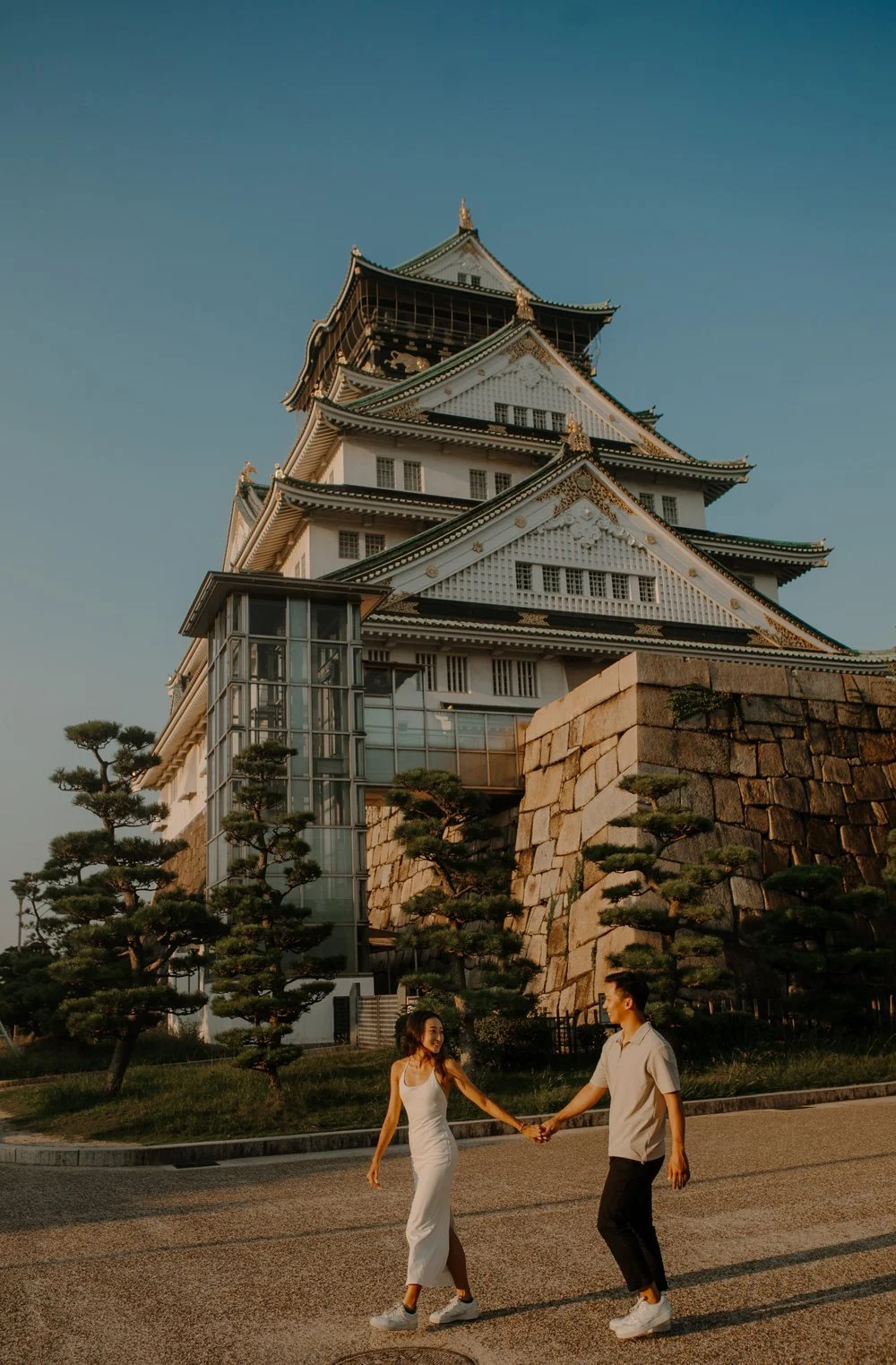 Couple walking hand in hand with Osaka Castle's stone walls and main tower behind them