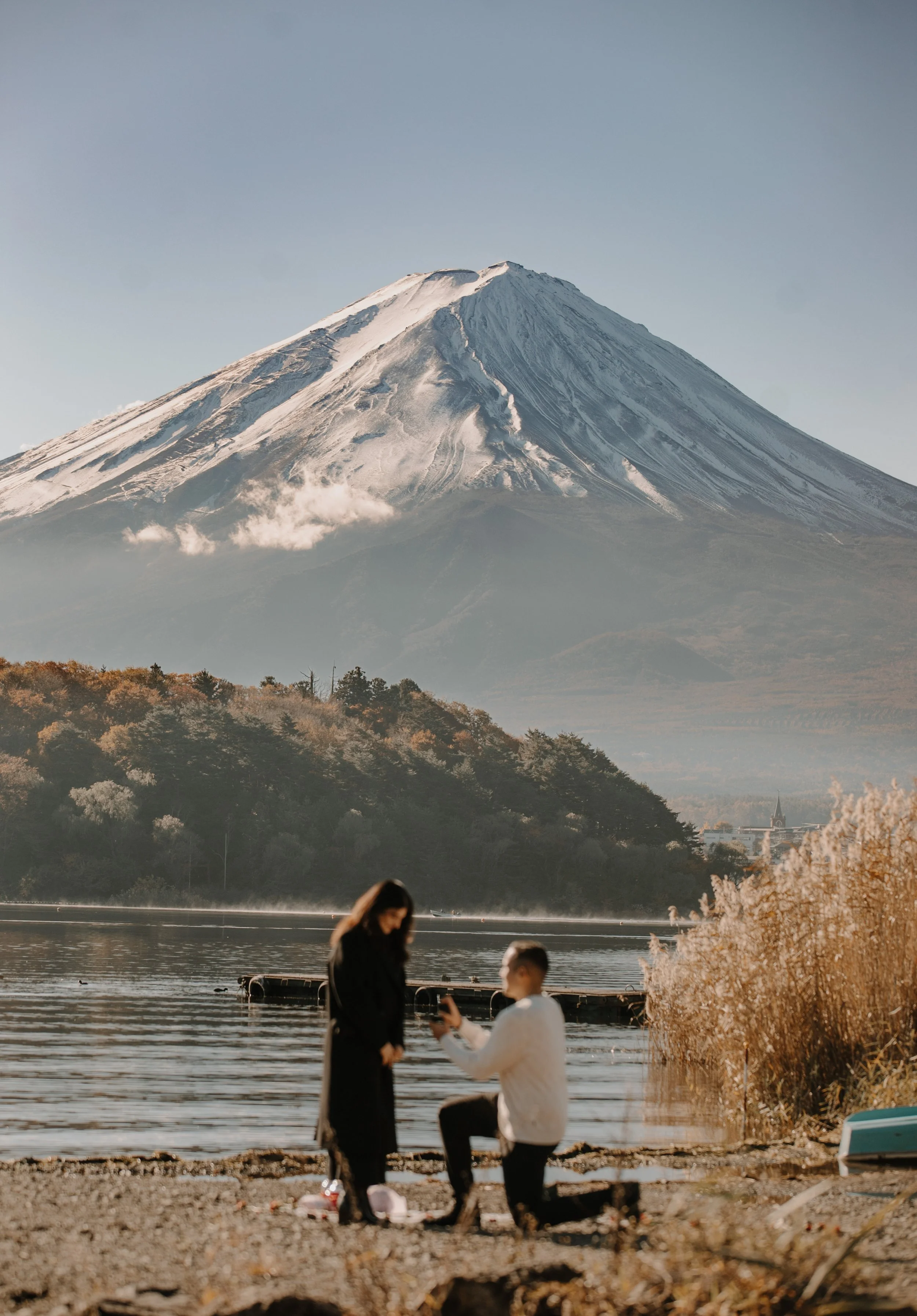 Man presenting a ring while kneeling in proposal at Lake Kawaguchiko at dawn with Mount Fuji in the background