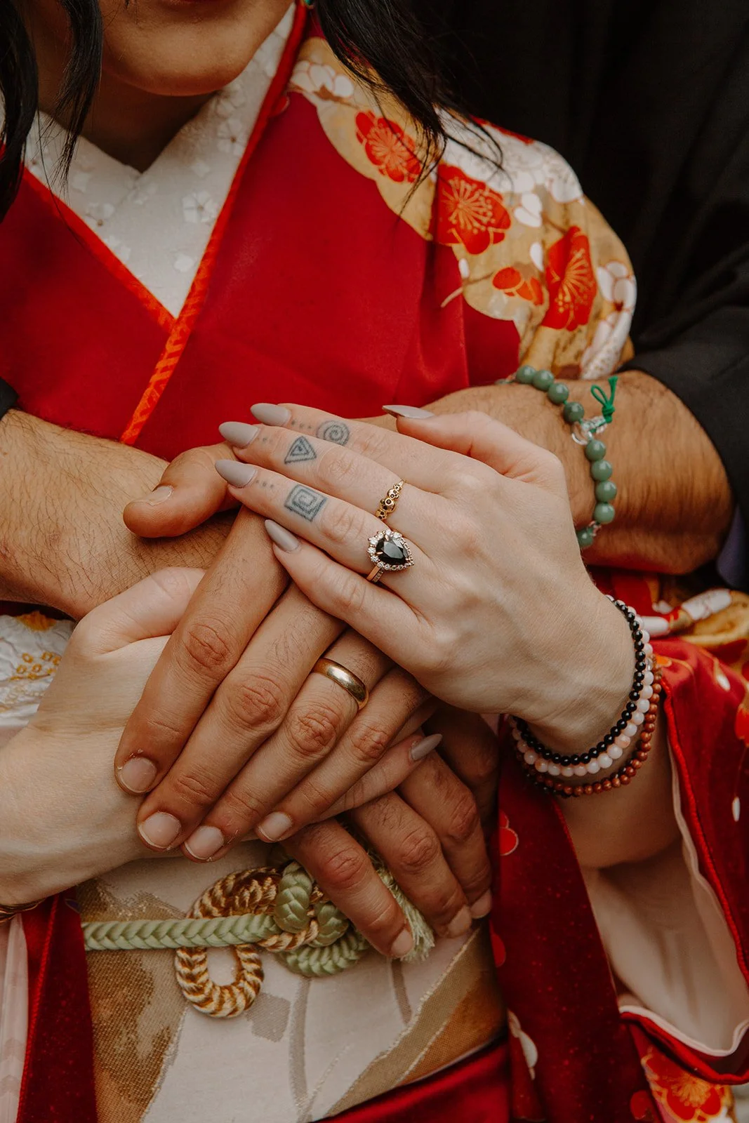 Close-up of the couple's clasped hands and wedding rings against red and gold kimono fabric.