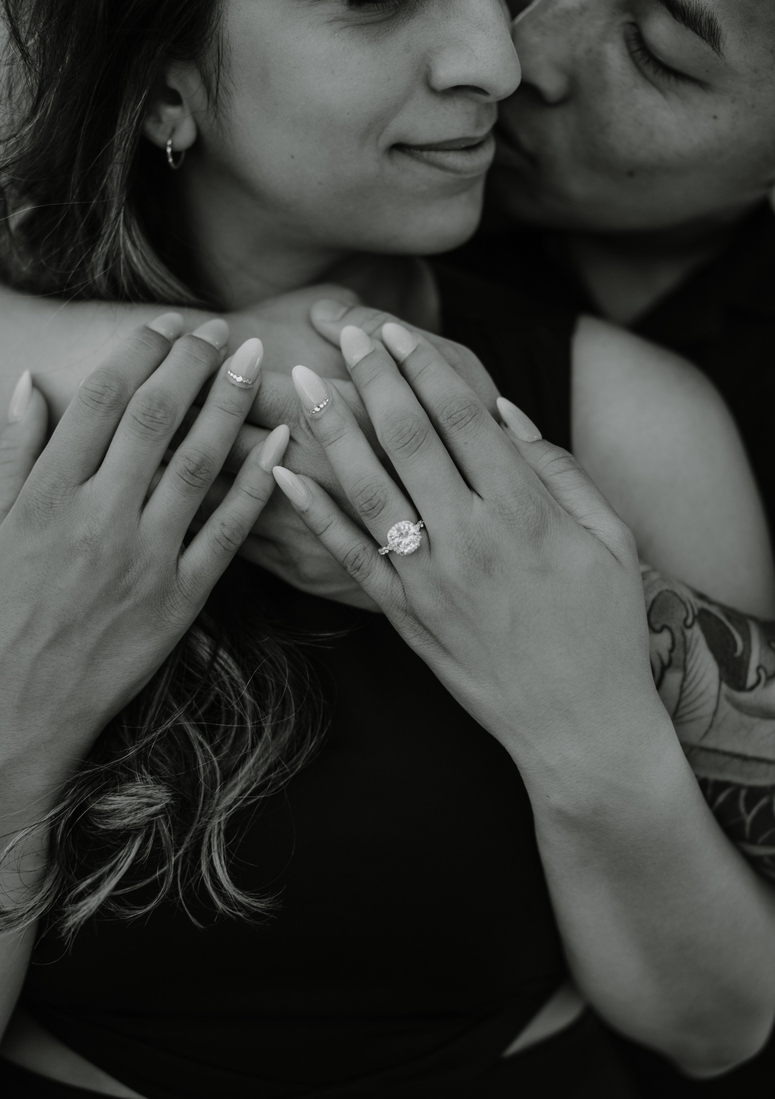 Black and white close-up of a couple kissing with the woman's engagement ring visible on her hand