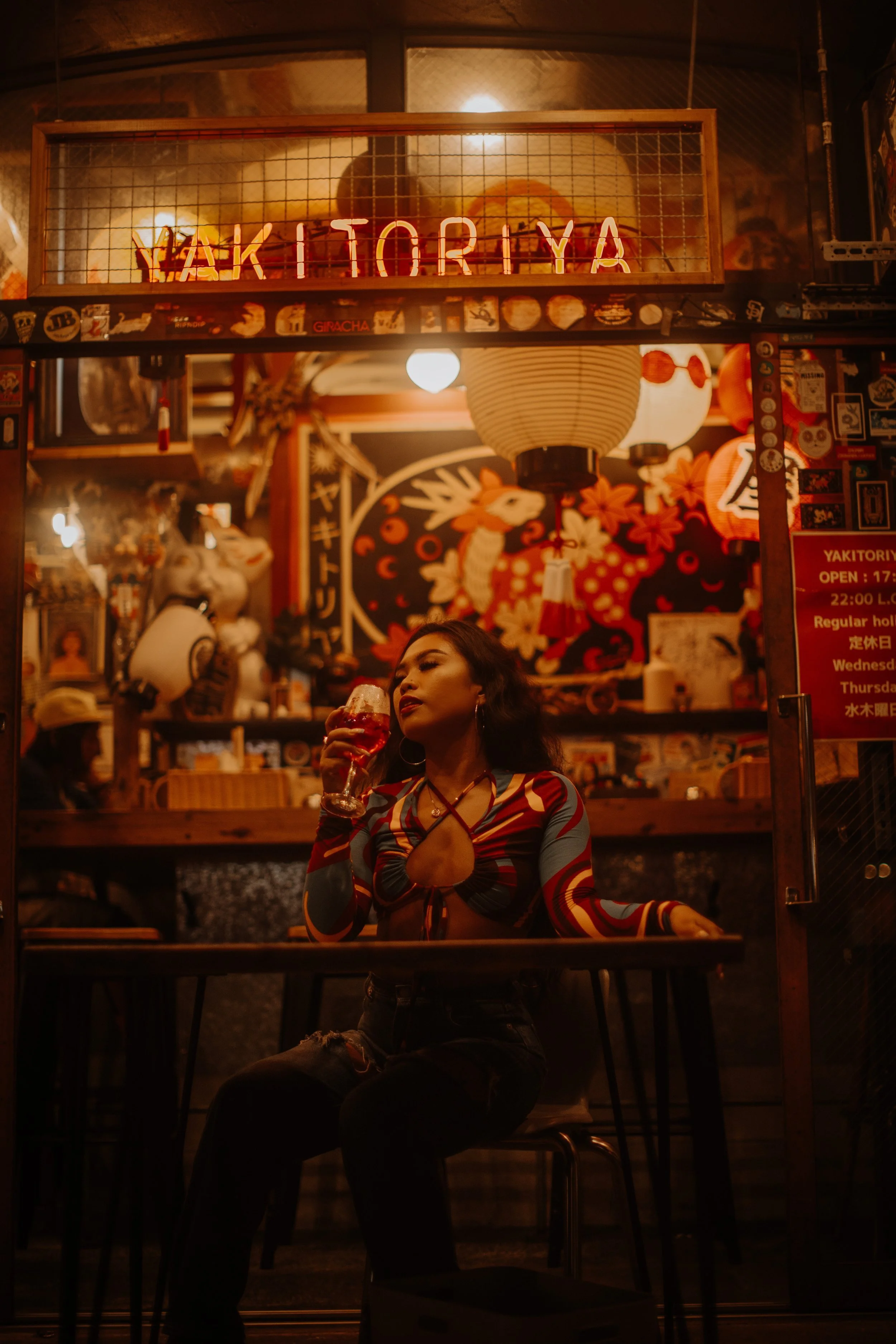 Woman sipping wine at a neon-lit Tokyo izakaya bar counter during an evening portrait session.
