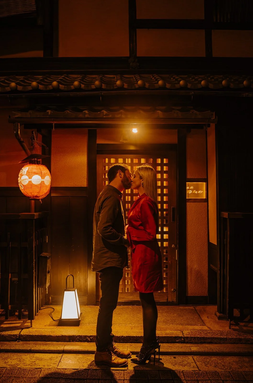 Couple kissing beneath a glowing red lantern outside a traditional Kyoto ryokan at night