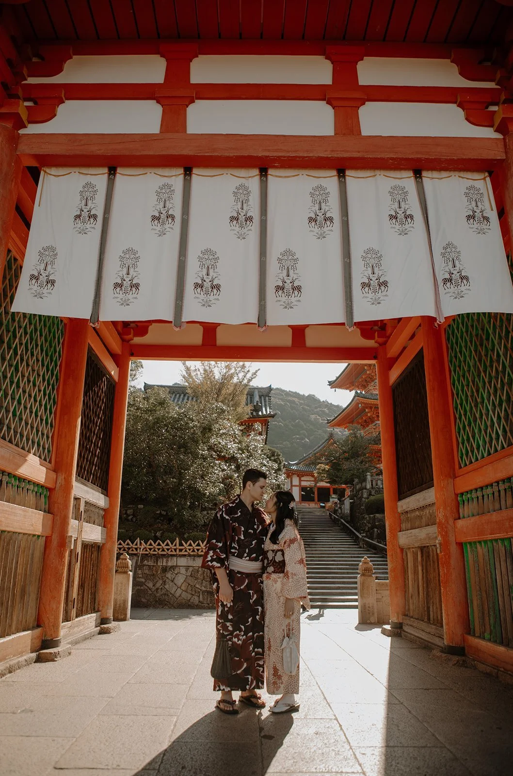 Couple in kimono standing close together under a vermilion temple gate curtain in Kyoto, Japan