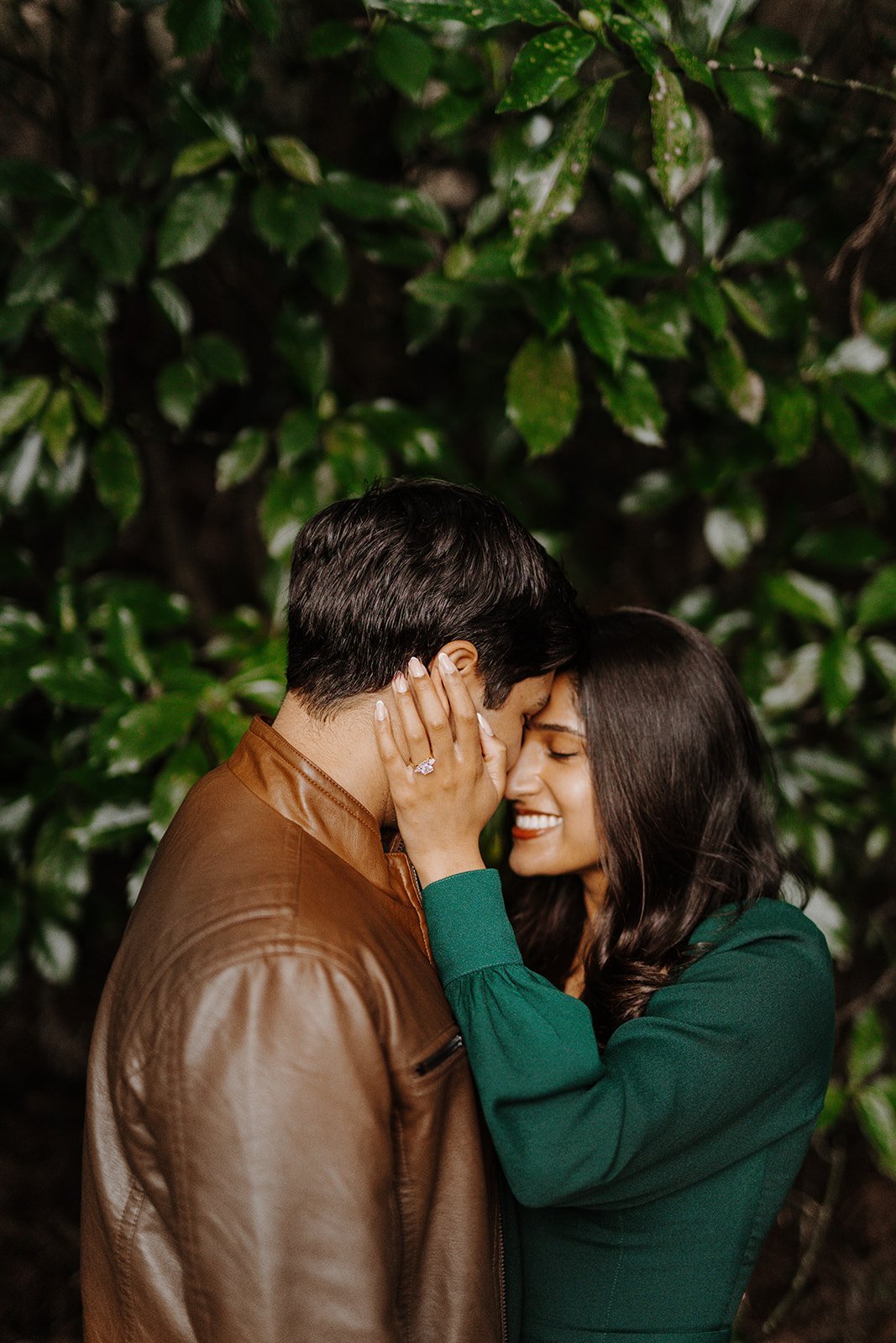 Newly engaged couple embracing forehead to forehead among dense greenery, her engagement ring visible on his face, Hakone