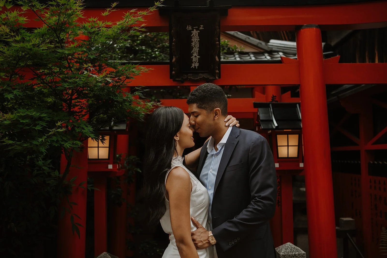 Couple kissing beneath a red shrine gate and lanterns in Gion, Kyoto in the evening