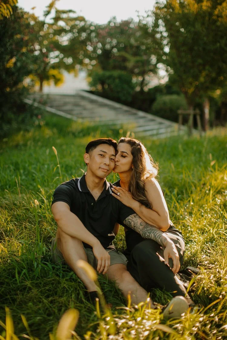 Couple sitting in the grass sharing a cheek kiss in a park near Osaka Castle at sunset