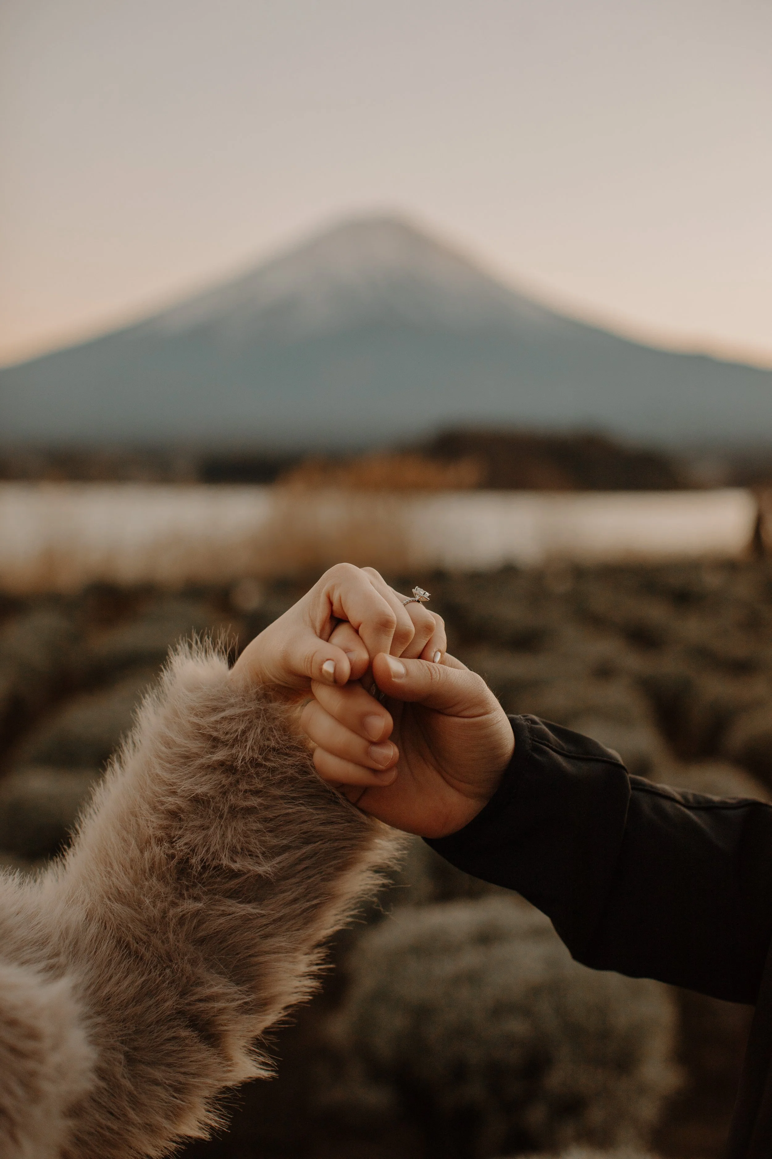 Close-up of a couple's clasped hands showing an engagement ring with Mount Fuji softly blurred behind