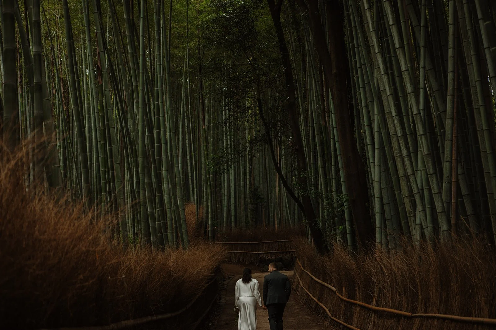 Bride and groom walking hand in hand along the path through the Arashiyama bamboo grove during a Kyoto elopement in Japan