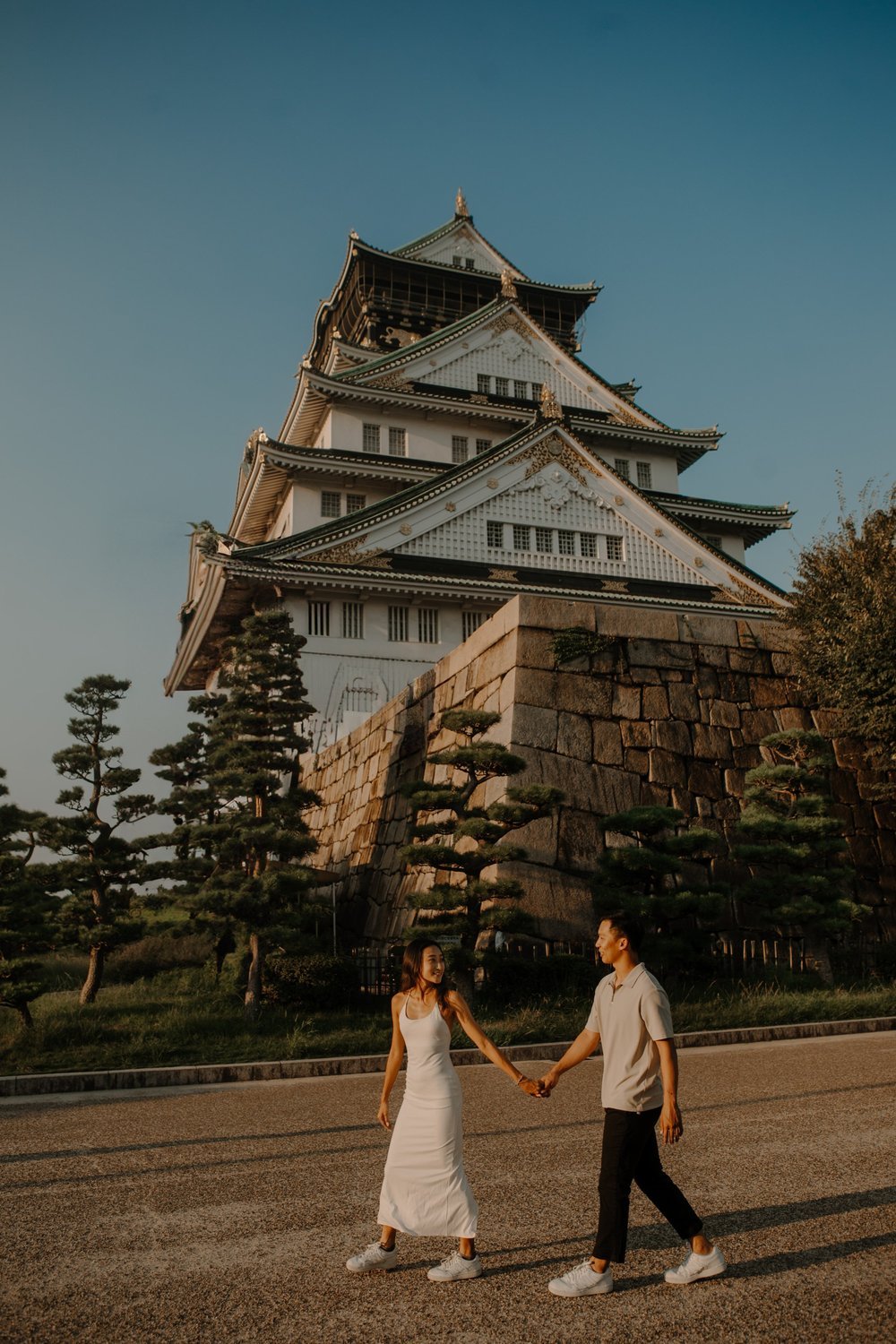 Couple in a white dress and light shirt walking hand in hand before Osaka Castle
