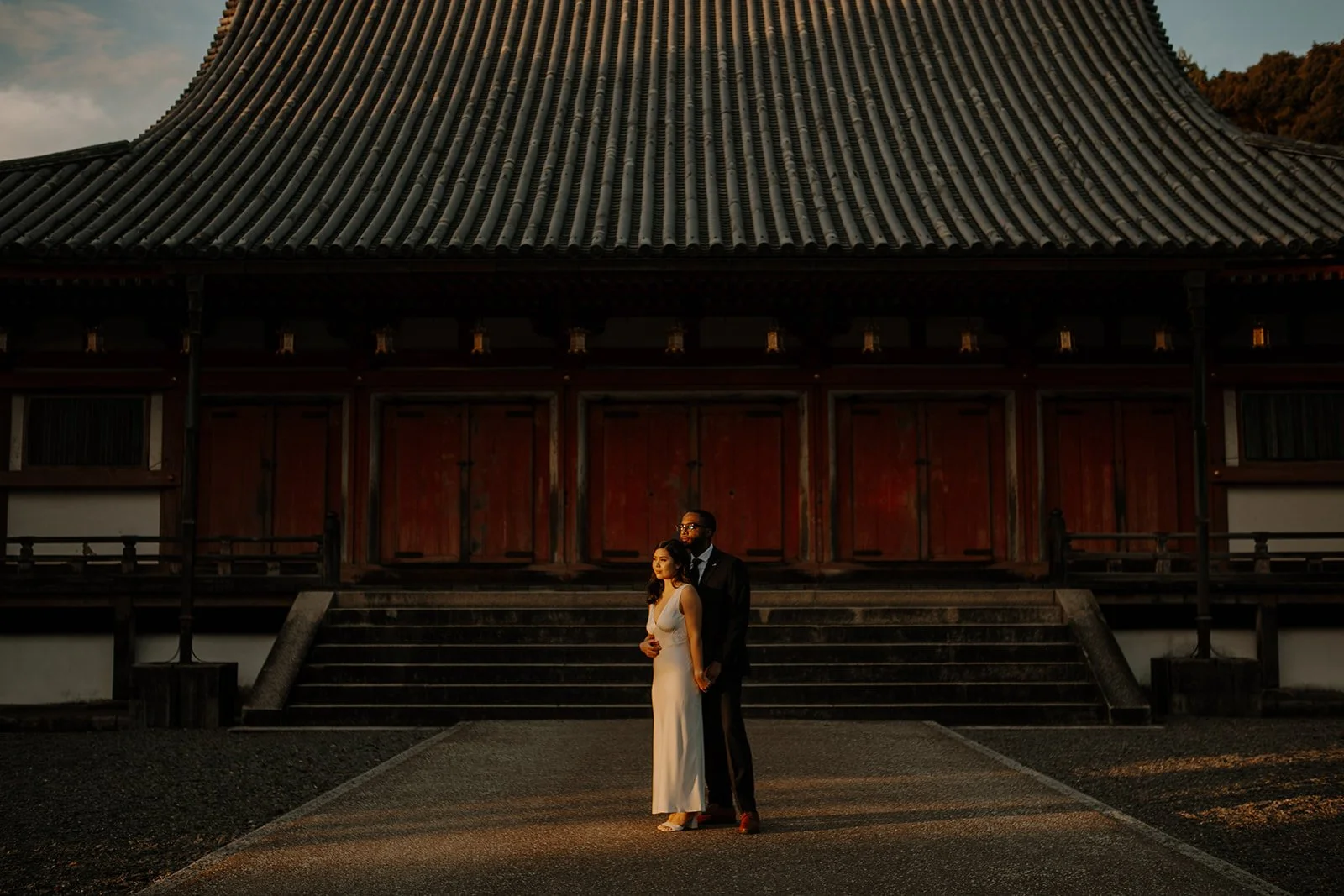 Bride and groom stand before Daigo-ji's weathered wooden temple hall at golden hour, Kyoto.
